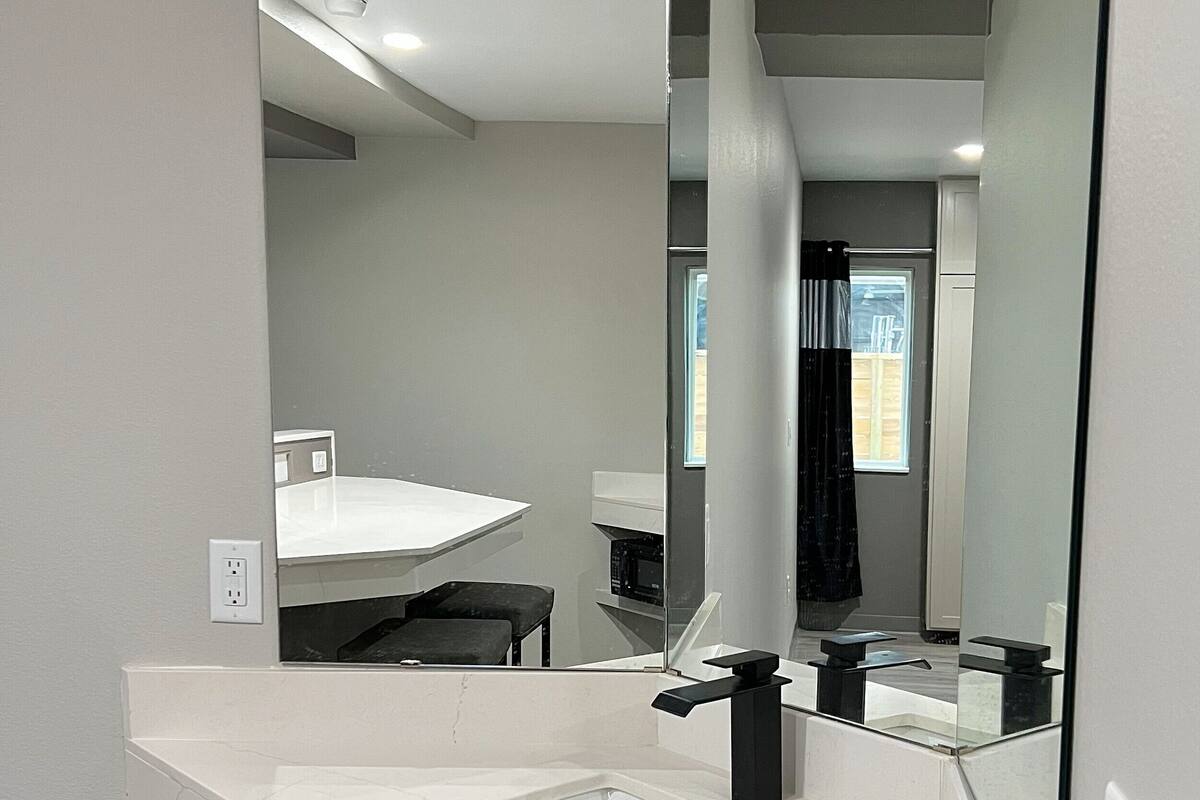 A modern bathroom with a large mirror, white marble countertop, and a visible shower area.