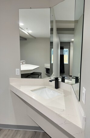 A modern bathroom with a large mirror, white marble countertop, and a visible shower area. - Crystal Inn Missouri City (Houston)
