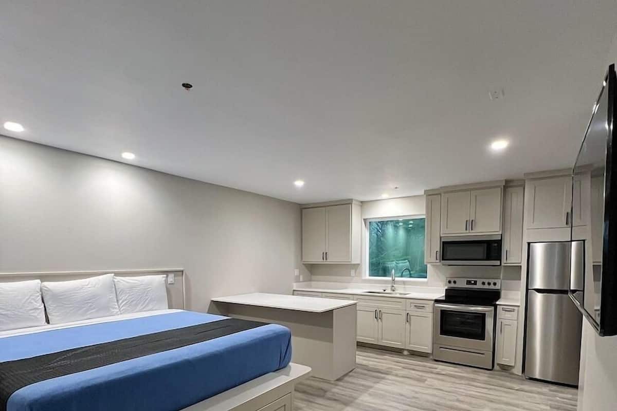 A modern bedroom with a bed, a small kitchenette with a microwave and refrigerator, and a window with a view.