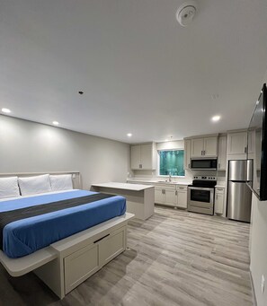 A modern bedroom with a bed, a small desk, and a kitchenette with a microwave, oven, and refrigerator. - Crystal Inn Missouri City (Houston)