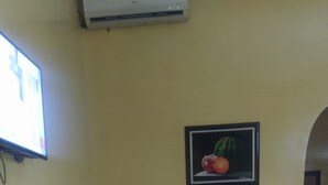 A dining area with a wooden table and chairs, a wall-mounted air conditioner, and a framed picture of a tomato. - Sky Suites Ikeja (Lagos)