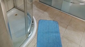 A bathroom with a glass shower enclosure, a white sink, a blue bath mat, and a towel hanging on a rack. - Sky Suites Ikeja (Lagos)