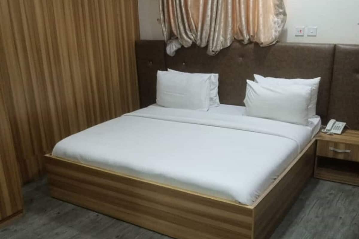 A hotel room with a wooden bed, white bedding, and a wooden floor.