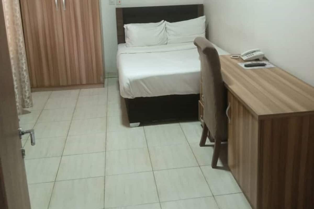 A small, neatly arranged bedroom with a bed, a wooden desk, and a wardrobe.