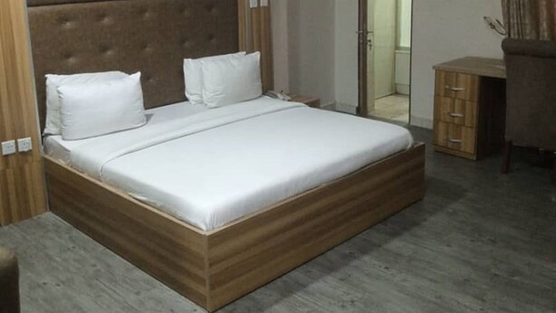 A bedroom with a large bed, wooden headboard, and a small wooden cabinet. - Sky Suites Ikeja (Lagos)