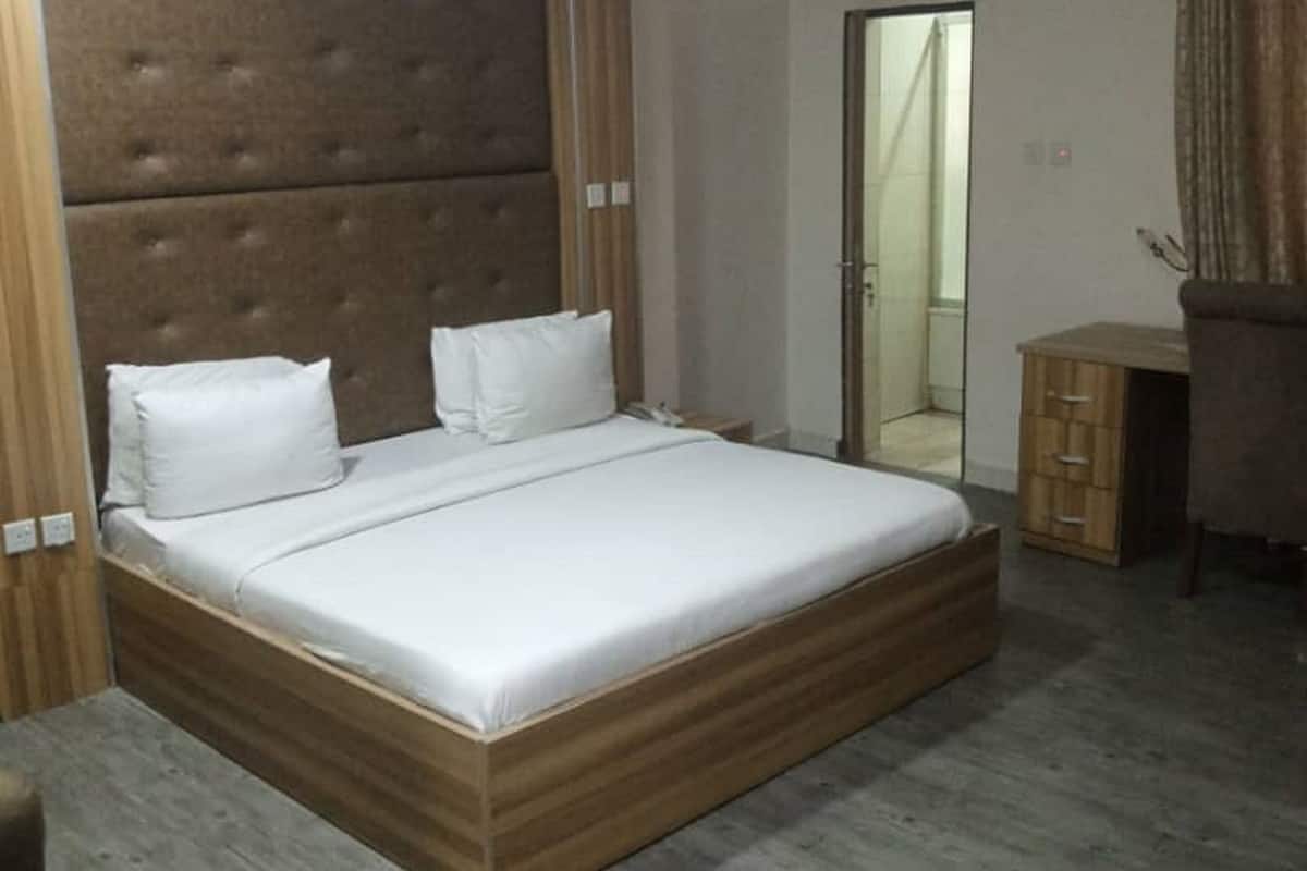 A bedroom with a large bed, wooden headboard, and a small wooden cabinet.