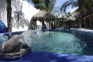 Una piscina con un mural de cebra, una estructura de techo de paja y un puente.