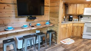 A compact kitchen with wooden cabinets, a built-in oven, and a small countertop with a coffee maker. - Juniper: Sleep 5, Tiny Cabin, Pets, Near Park/Lake (Broken Bow)