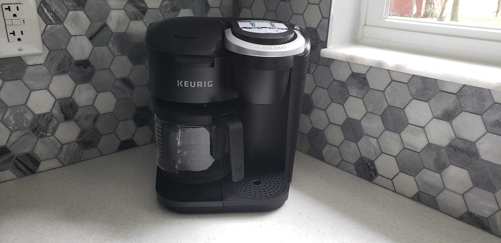 Una cafetera Keurig sobre una encimera de cocina con salpicadero de azulejos hexagonales.