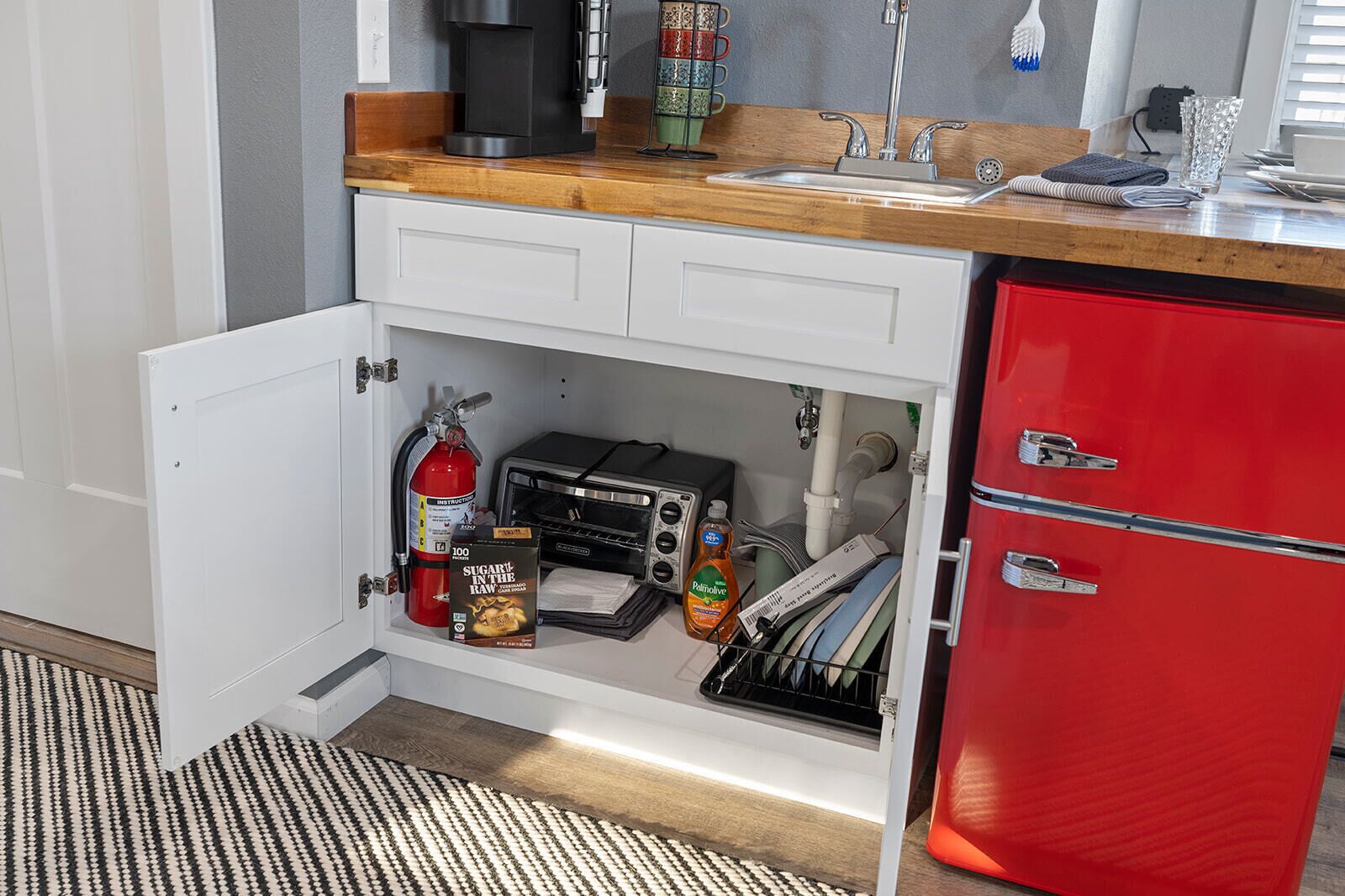 Una cocina con un refrigerador rojo, una tostadora, un extintor y una cafetera.