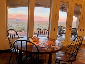 A dining area with a table and chairs, a puzzle on the table, and a view of a desert landscape through large glass doors. - Luxury Near Lake Powell & Antelope Canyon: Hot Tub, Views & EV Charger (Page)