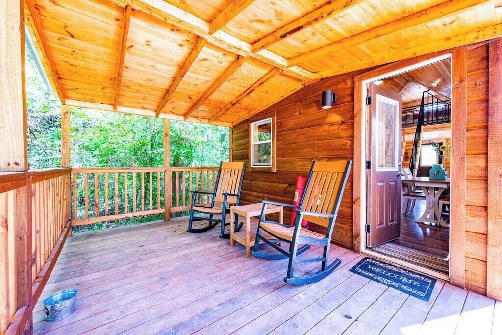 Une cabane en bois dotée d’une véranda, de fauteuils à bascule et d’une porte donnant sur un intérieur comprenant une table et des chaises.