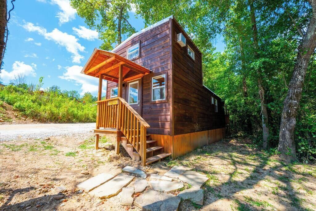 Une cabane en bois dotée d’une véranda, d’un escalier en pierre et surplombant une forêt.