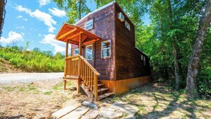 A wooden cabin with a porch, stone steps, and a forested backdrop. - Acorn: Sleeps 4, Tiny Cabin, Pets, Near Park/Lake (Broken Bow)