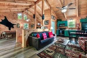 Interior de uma cabana de tronco com sala de estar, cozinha e sala de jantar.