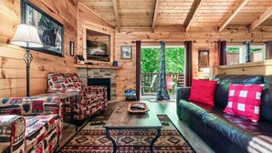 Un acogedor interior de cabaña con chimenea, un sofá, un sillón estampado y un televisor.