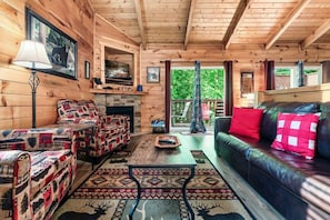 L’intérieur d’un chalet chaleureux, avec une cheminée, un canapé, un fauteuil à motifs et un téléviseur.