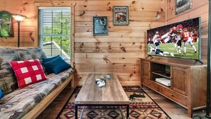 Interior de una cabaña de madera con sofá, mesa de centro, televisor y cuadros en las paredes.
