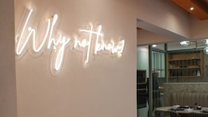 Een neonbord met de tekst 'Why not?' op een muur, een eetgedeelte met stoelen en een tafel, en een vloer met een patroon.