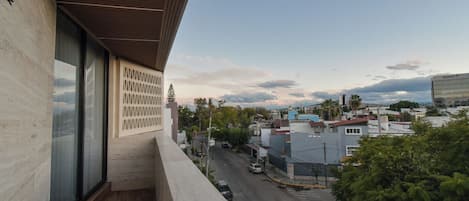 Um edifício moderno com grandes janelas e varanda com vista para uma rua com carros e edifícios.