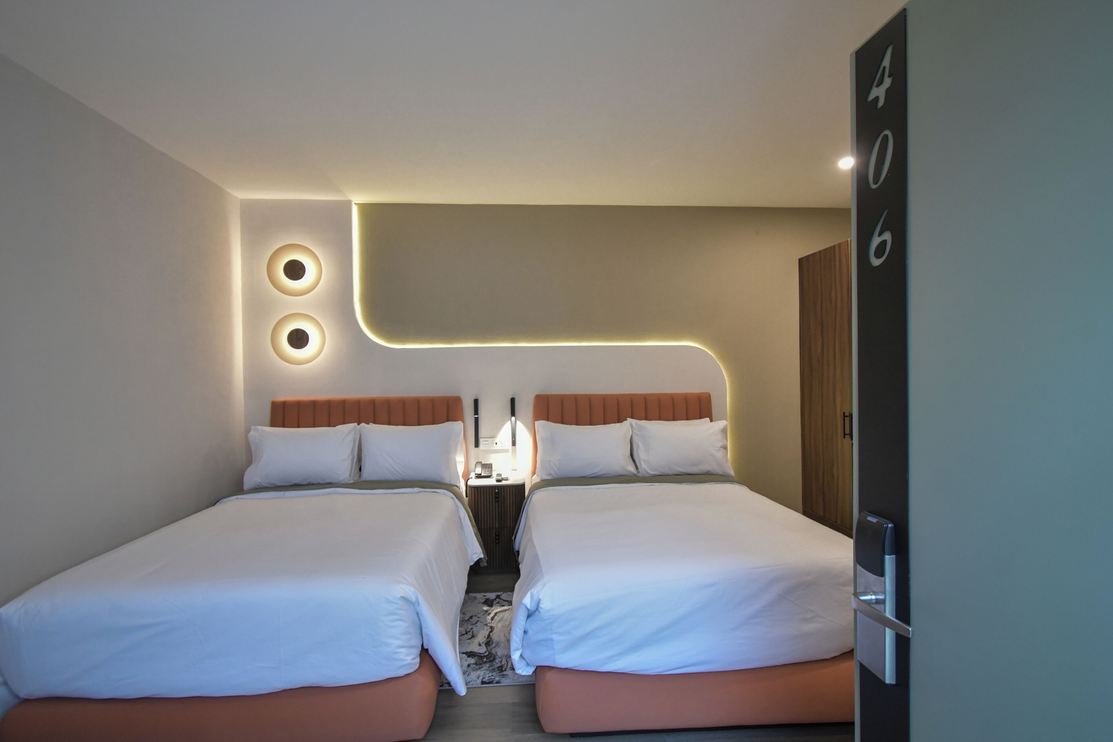 Habitació d'hotel amb dos llits, una tauleta de nit i un senyal numèric penjat a la paret.