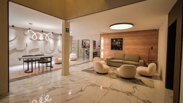 Een moderne lobby met een marmeren vloer, een glazen tafel met stoelen, een bank en een muur met abstracte kunst.