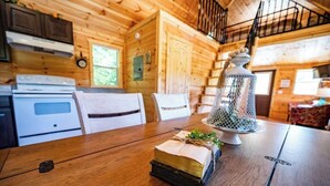 Interior de uma cabana de madeira com mesa de jantar, cadeiras, fogão e luminária pendente.