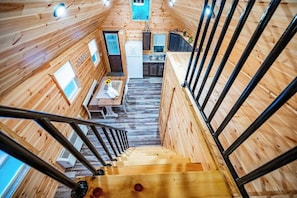 A wooden cabin interior with a staircase, a kitchen area, and a dining space.
