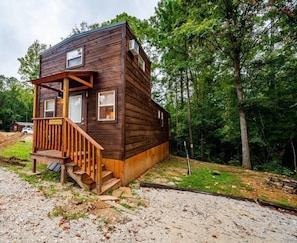 Escape to a serene cabin surrounded by dense trees, with a cozy porch and a wooden staircase leading to the entrance.