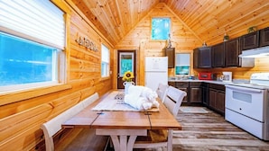 Ein Holzblockhaus-Interieur mit Esstisch, Stühlen, einem Kühlschrank und einer Küchenzeile.