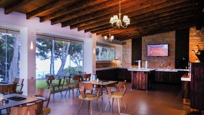 Un interior moderno con vigas de madera en el techo, una zona de bar con televisor y un comedor con sillas y mesas.