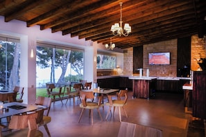 Un interior moderno con vigas de madera en el techo, una zona de bar con televisor y un comedor con sillas y mesas.