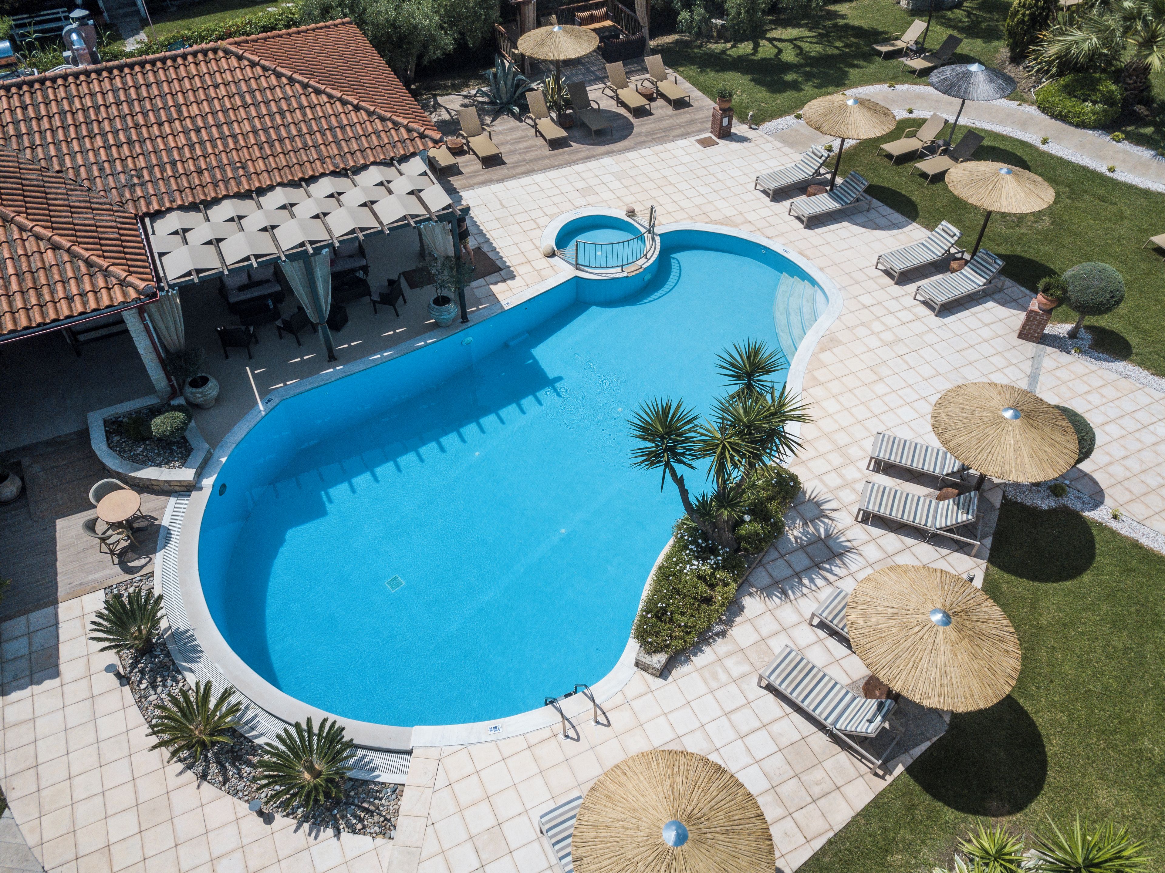 An aerial view of a swimming pool with lounge chairs and umbrellas, surrounded by a patio area and greenery.
