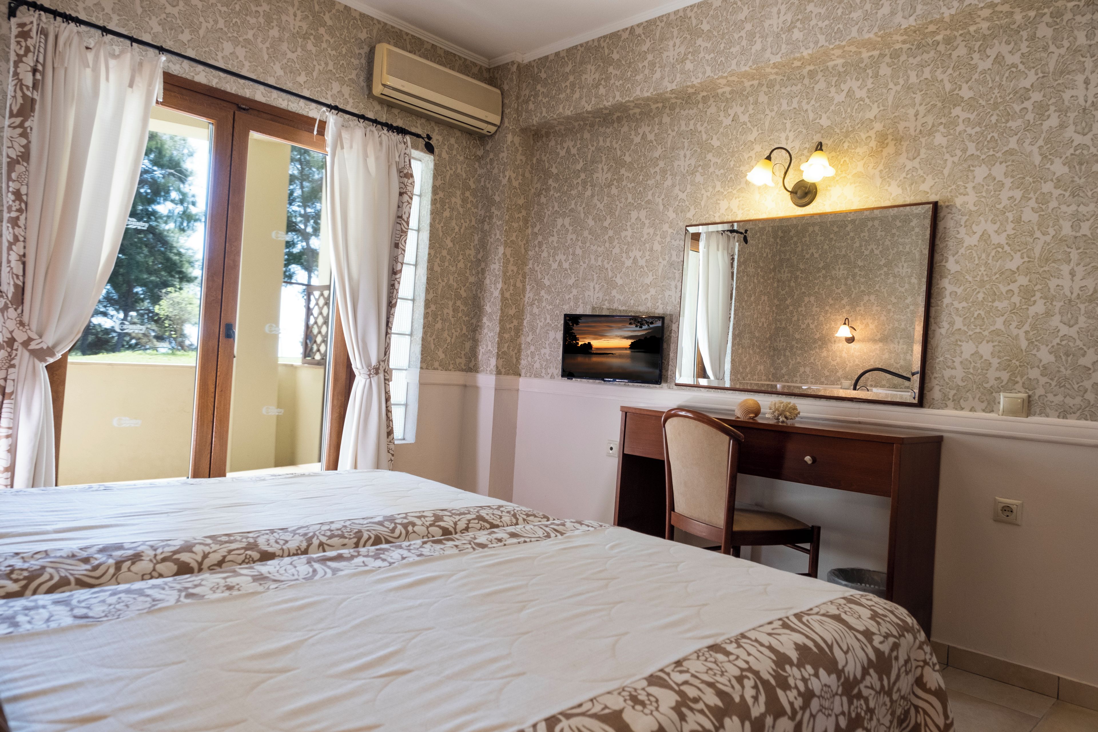 Ein Hotelzimmer mit einem großen Bett, einem Schreibtisch mit Stuhl, einem Fernseher und einem Fenster mit Vorhängen.
