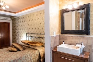 Un dormitorio con cama, almohadas y cabecera. La habitación tiene papel tapiz y una puerta de madera.