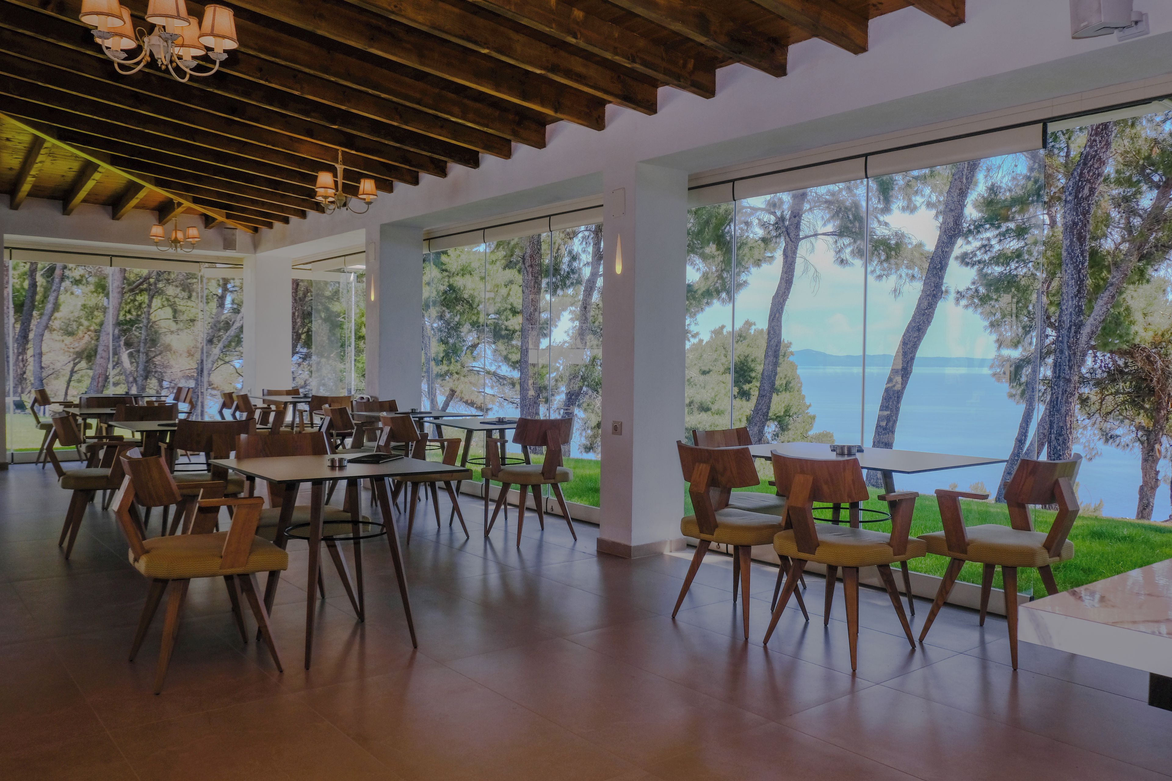 Un comedor amplio con mesas y sillas de madera, grandes ventanas que ofrecen vistas a árboles y agua.
