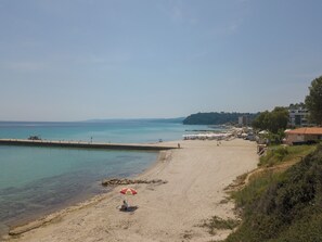 Ein Strand mit sandigem Ufer, einem Steg und einer Reihe von Gebäuden im Hintergrund.