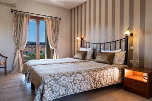 A double bed with floral bedding, a nightstand with a lamp, and a view through a window with curtains. - Country Inn (Kassandra)