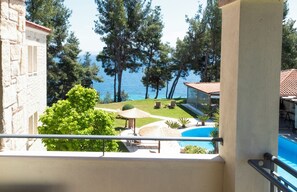 Un balcón con vista a una piscina, sillones de descanso y un área verde con árboles.