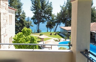 Un balcón con vista a una piscina, sillones de descanso y un área verde con árboles.