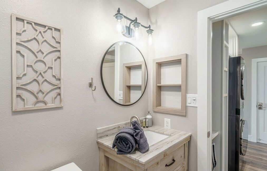 Un baño con lavamanos de mármol, un espejo redondo, un panel decorativo en la pared y una zona de ducha visible a través de una puerta abierta.