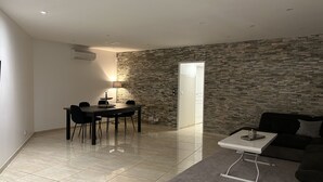 Ein modernes Wohnzimmer mit Essbereich, Steinwand, Fliesenboden und einem an der Wand befestigten Flachbildfernseher.