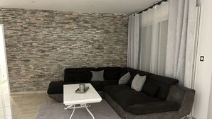Ein modernes Wohnzimmer mit einem Ecksofa, einem kleinen weißen Tisch und einer Wand mit Steinmuster.
