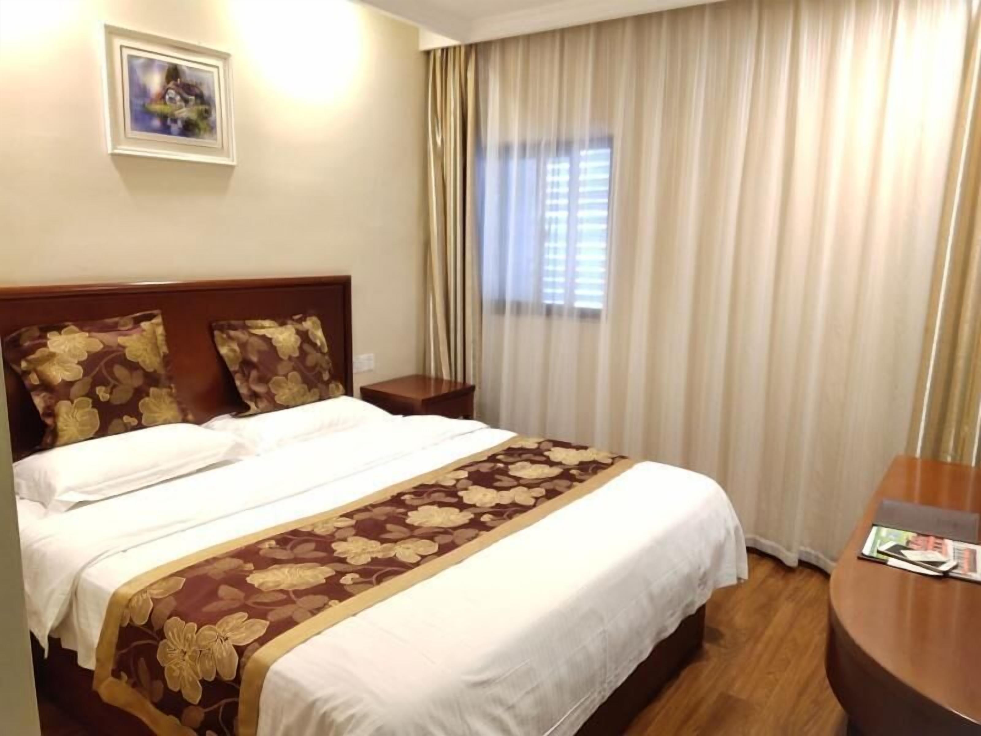 A hotel room with a large bed, a wooden headboard, a nightstand, a round table, and a window with curtains.