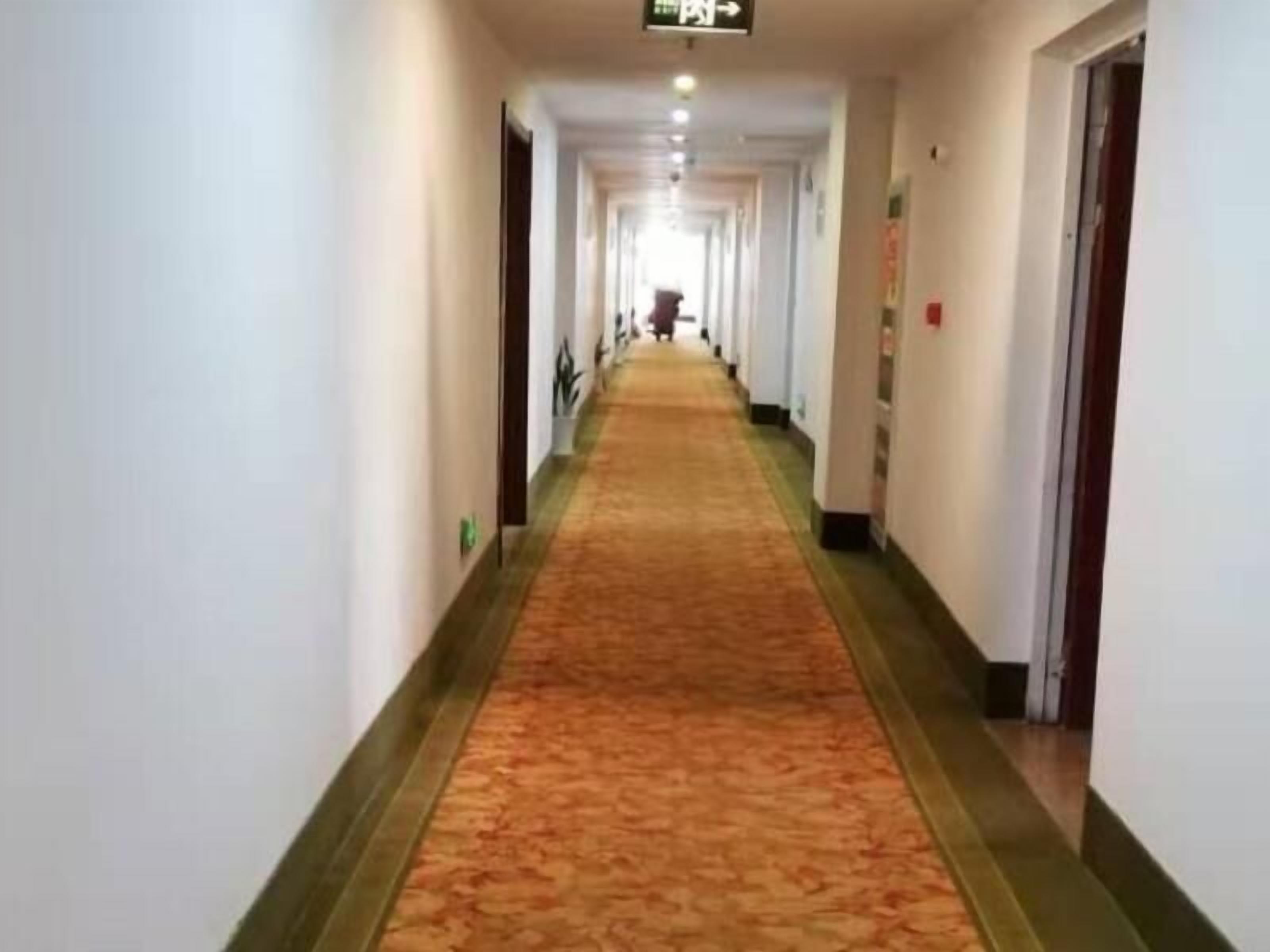 A long, narrow hotel corridor with a carpeted floor and doors on both sides.