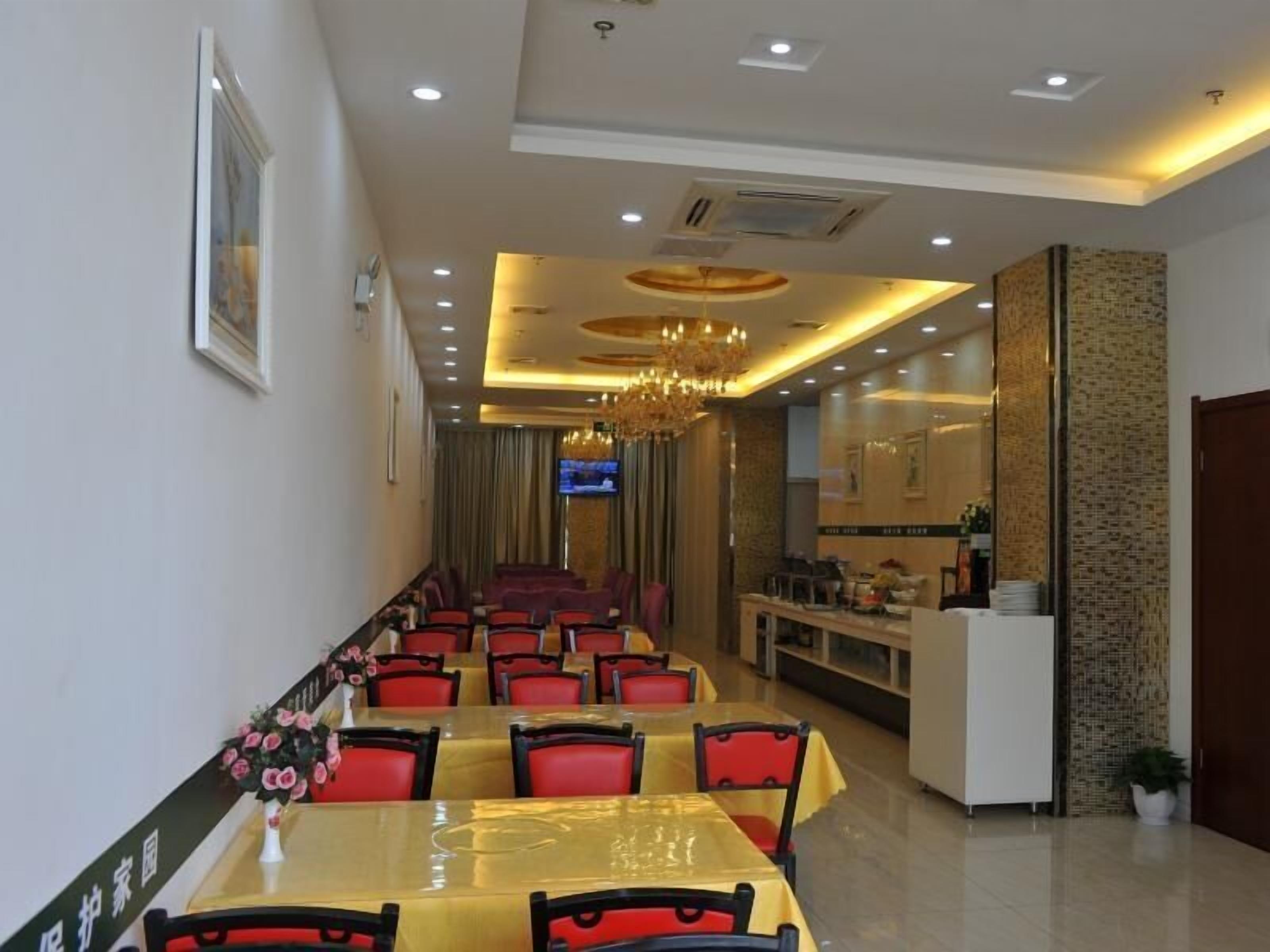 Un restaurant avec une longue table à manger, des chaises rouges, un lustre et un téléviseur fixé au mur.