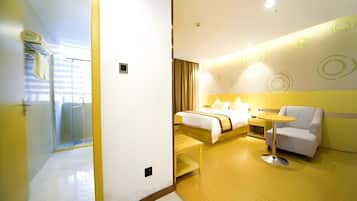 Una habitación de hotel moderna con cama, una mesita, una silla y zona de ducha con paredes de vidrio.