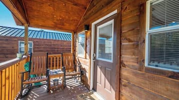 A wooden porch with a door, two chairs, and a small table.