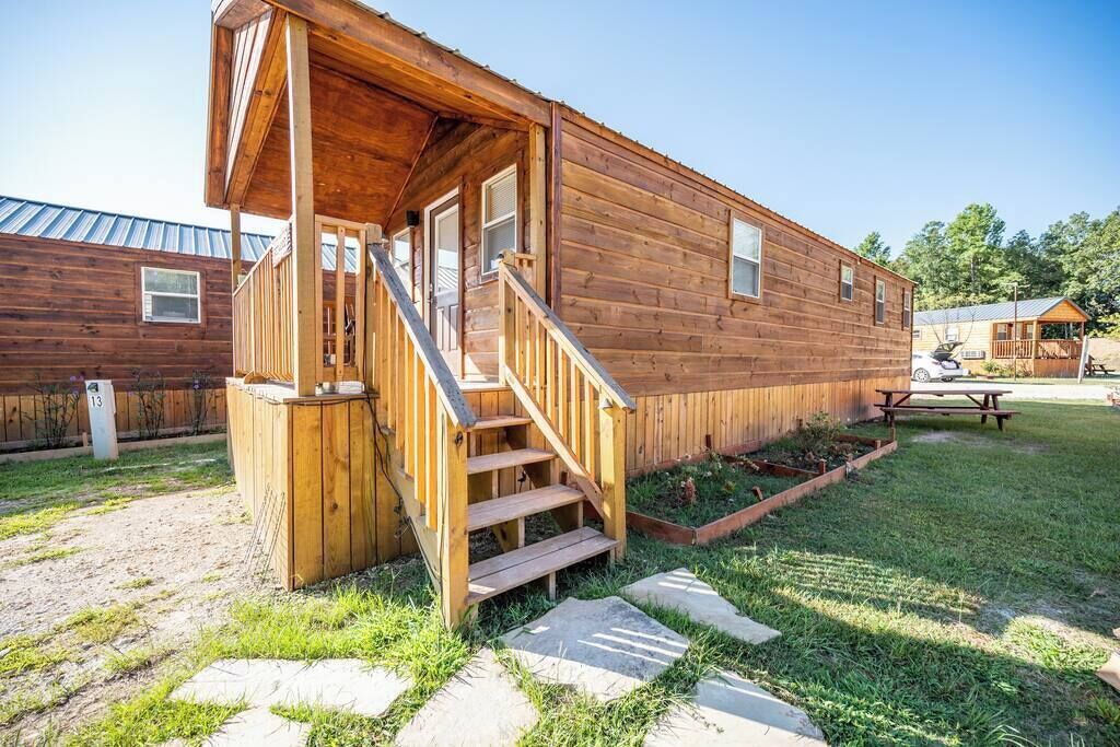 A wooden cabin with a porch, a staircase, and a picnic table in the yard.
