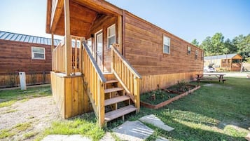 A wooden cabin with a porch, a staircase, and a picnic table in the yard.